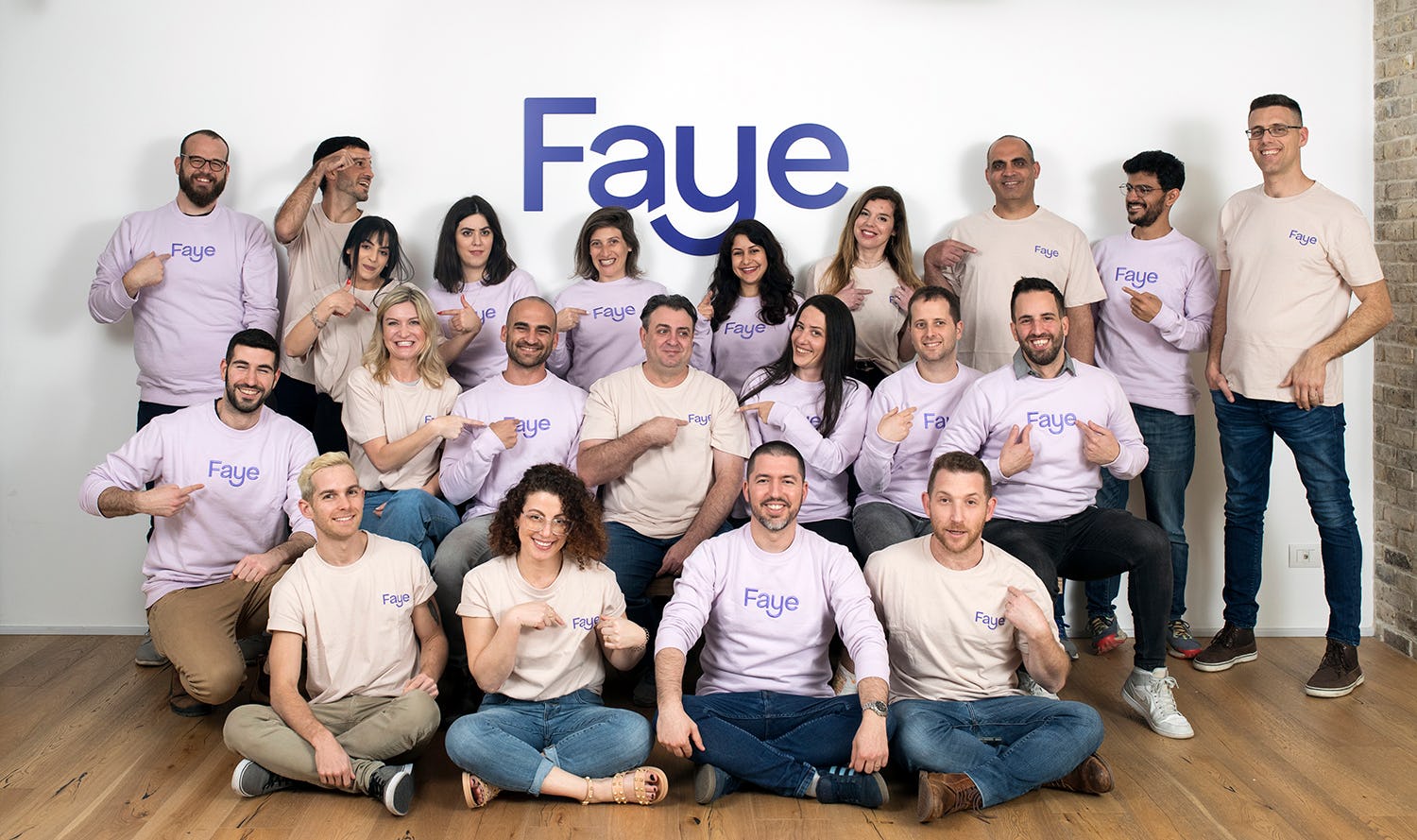 Faye team wearing Faye shirts and sweatshirts in front of the Faye sign