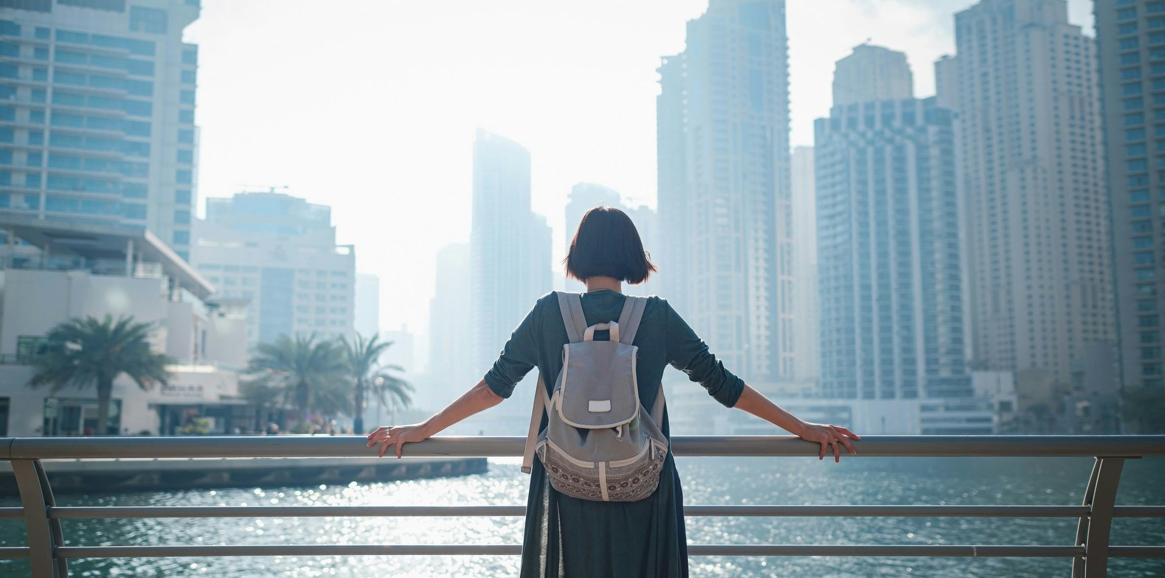 Girl with a backpack holding a railing and looking into the city