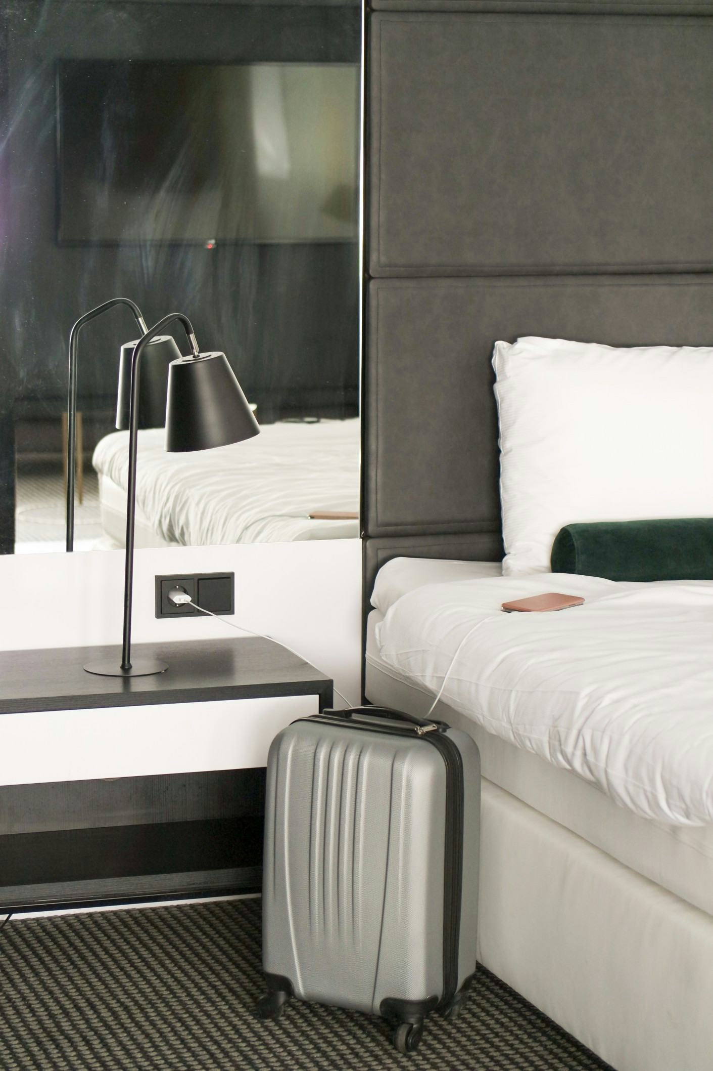 silver carry on suitcase next to phone plugged in to charger in a hotel room
