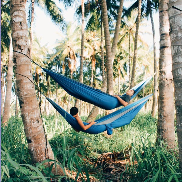 2 men in blue hammocks hanging between trees