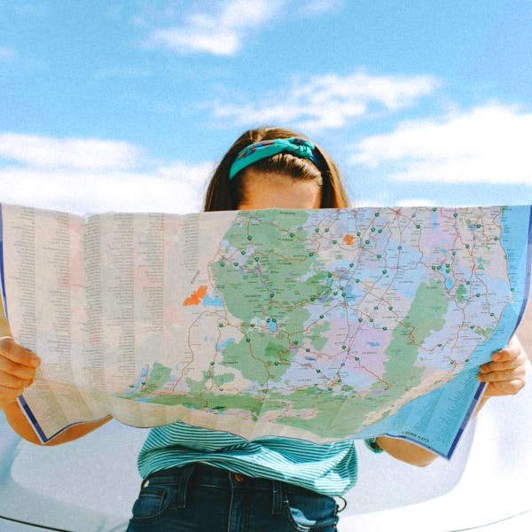 Girl with a blue shirt and headband looking at a map with a car and landscape behind her