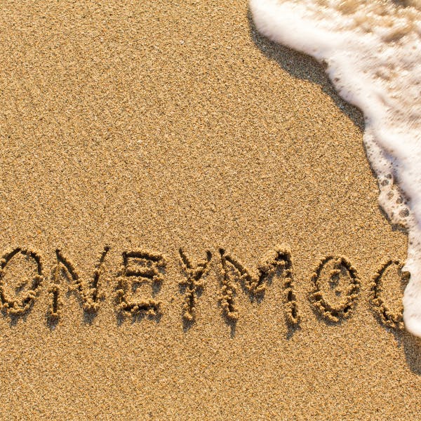 The word "honeymoon" written in the sand with the ocean water coming up.