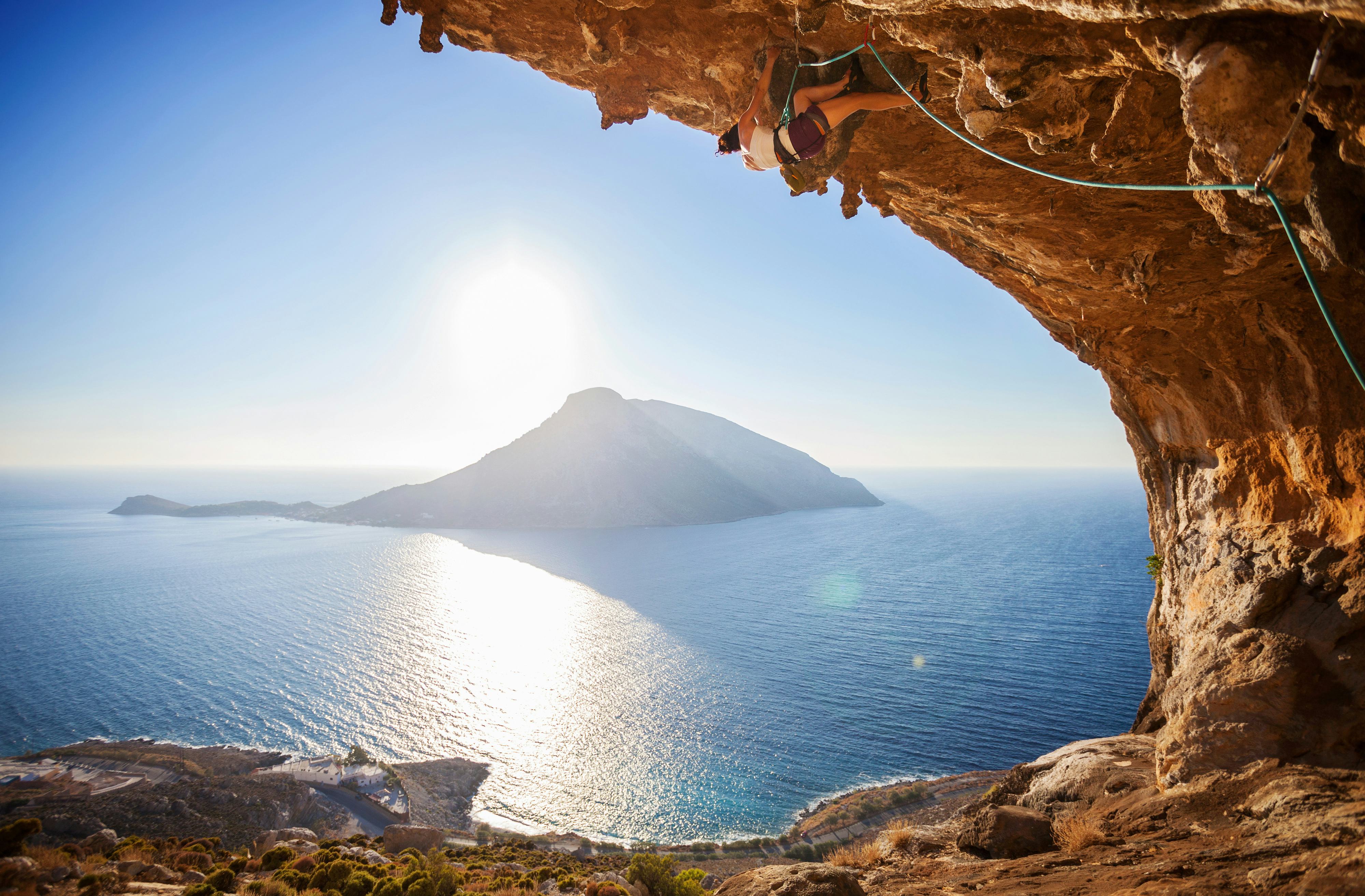 Female rock climber climbing along roof in cave in Kalymnos, Greece