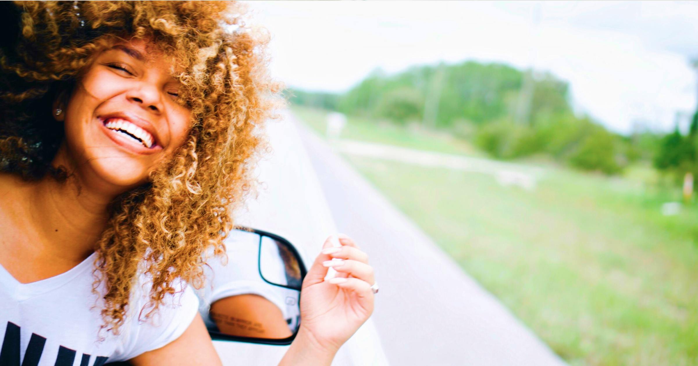 Woman with luscious curly hair smiling with her head out a car window