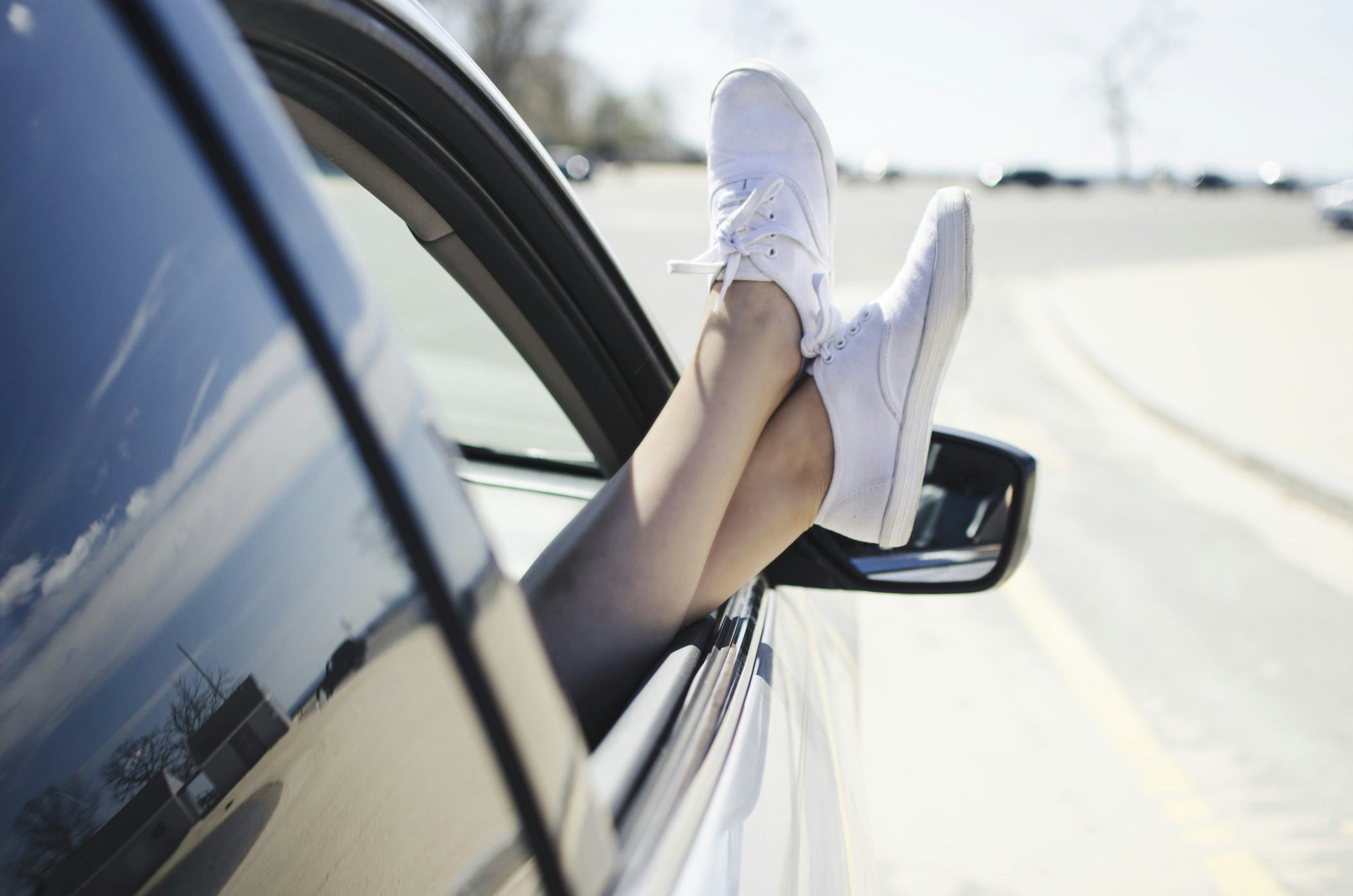 girl in a car on a road trip with her while sneakers hanging out the window