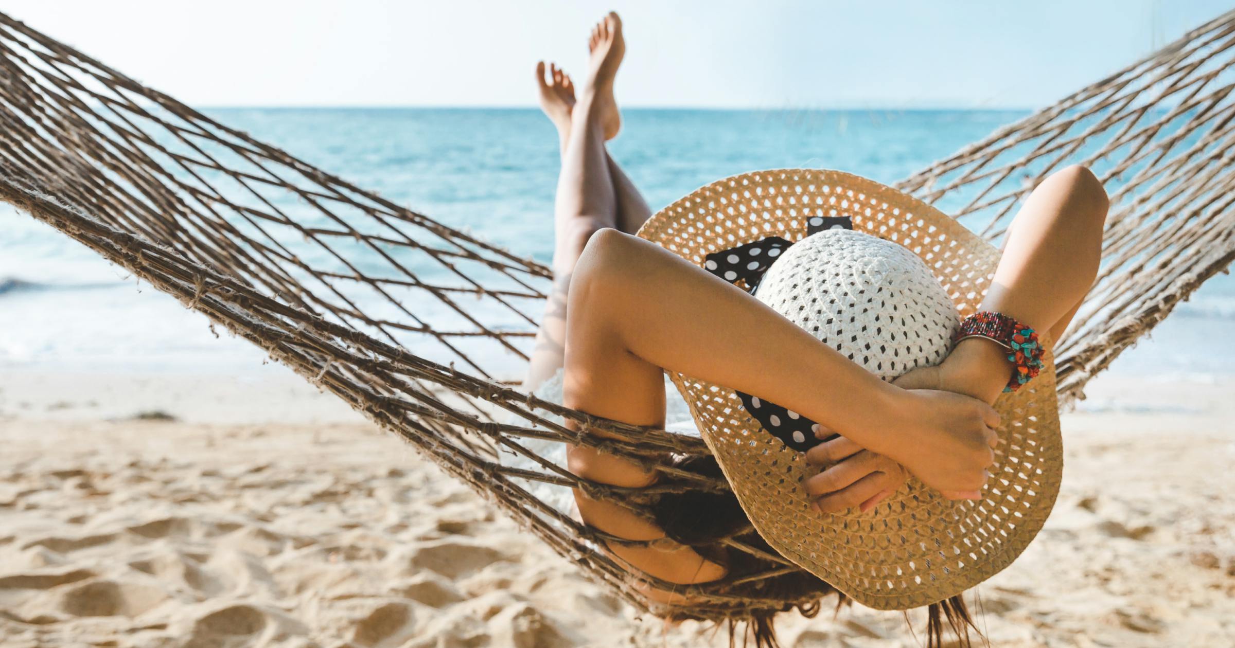 Woman in a wide brim hat on a hammock on the beach overlooking the ocean
