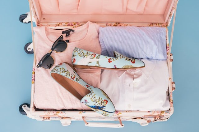 Open pink suitcase with some clothes, cute loafers and sunglasses 