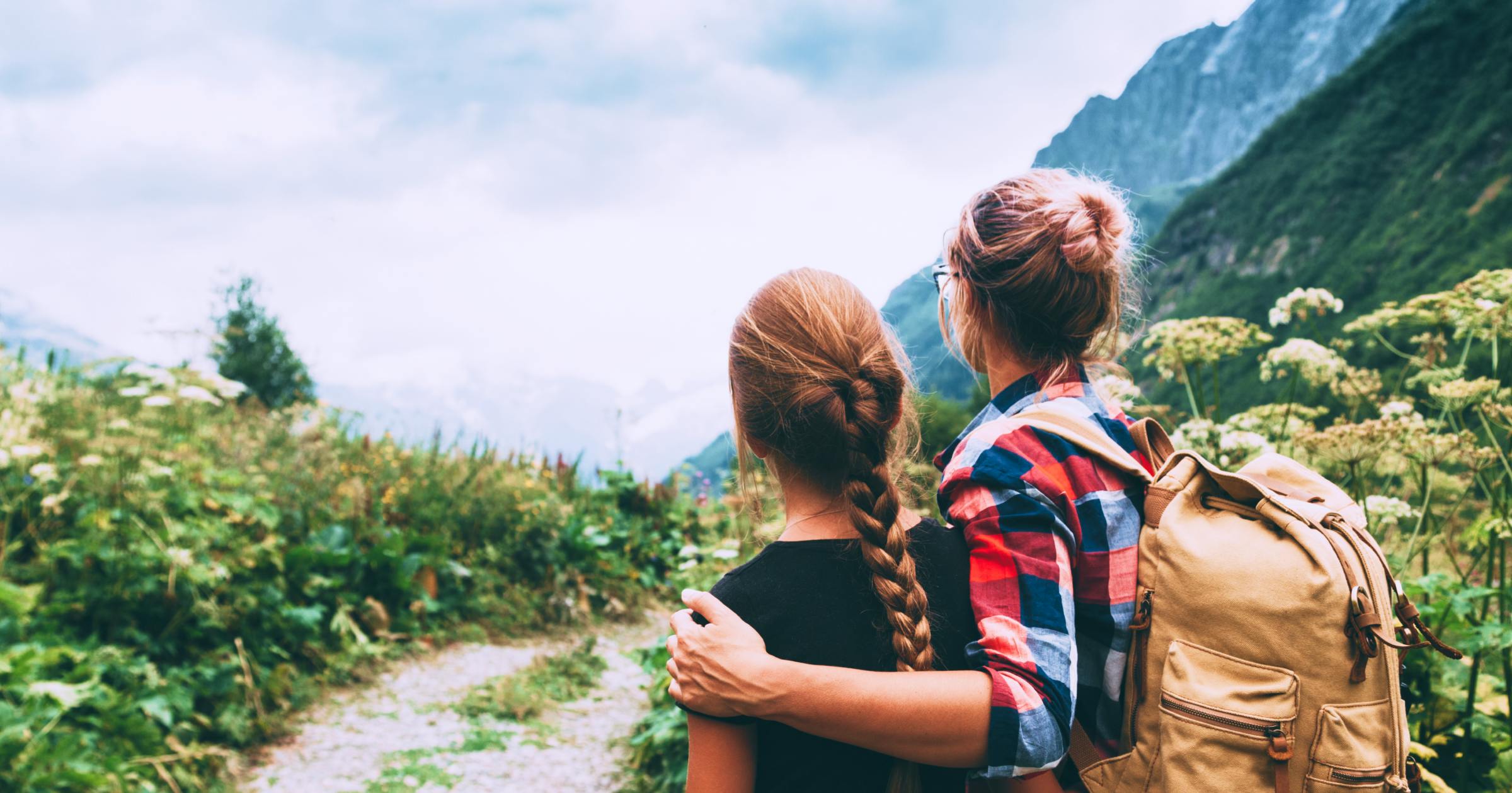 Mom with arm around teen daughter looking at mountains in front of them.