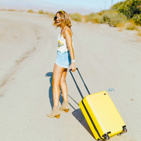 woman smiling on beach with yellow carry-on suitcase 