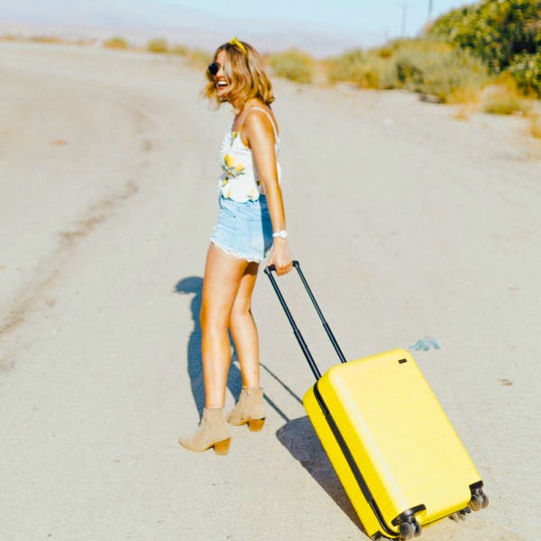 woman smiling on beach with yellow carry-on suitcase