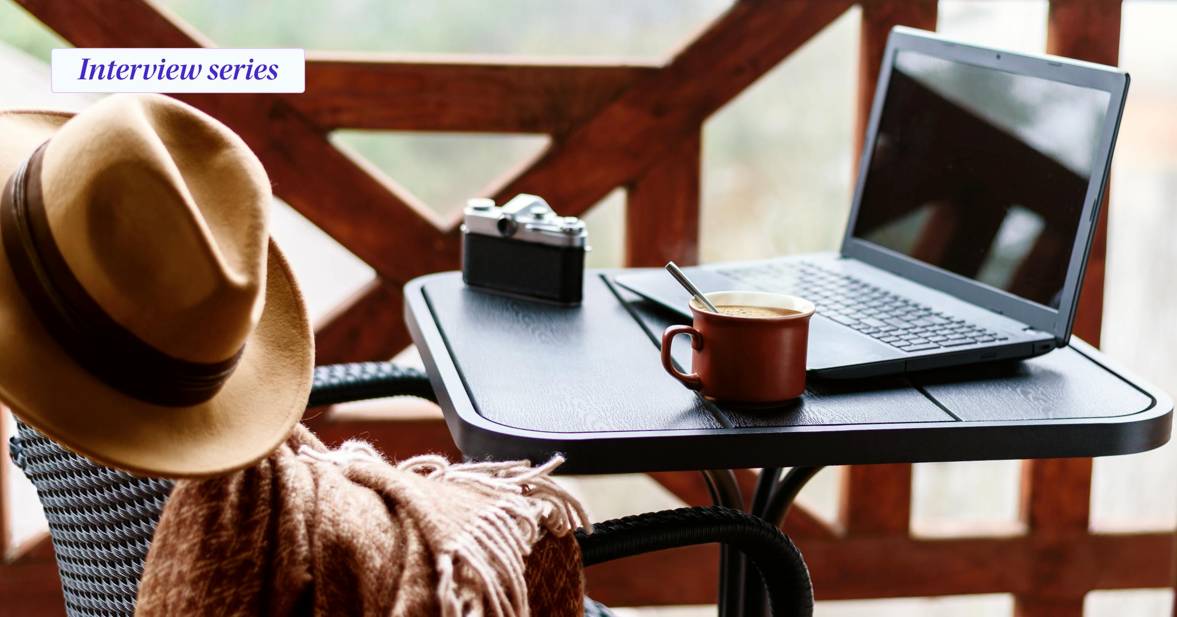 Computer, coffee cup, a camera on a table with a hat and scarf sitting on a chair with the tag interview series on the top left