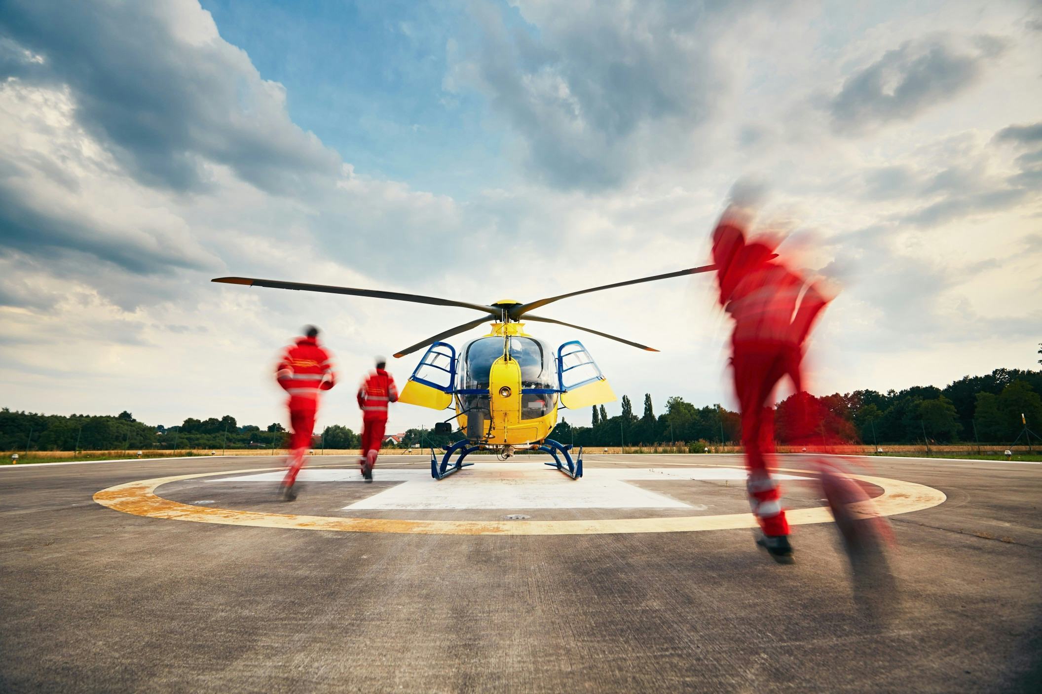 3 people in orange uniforms running towards a yellow helicopter