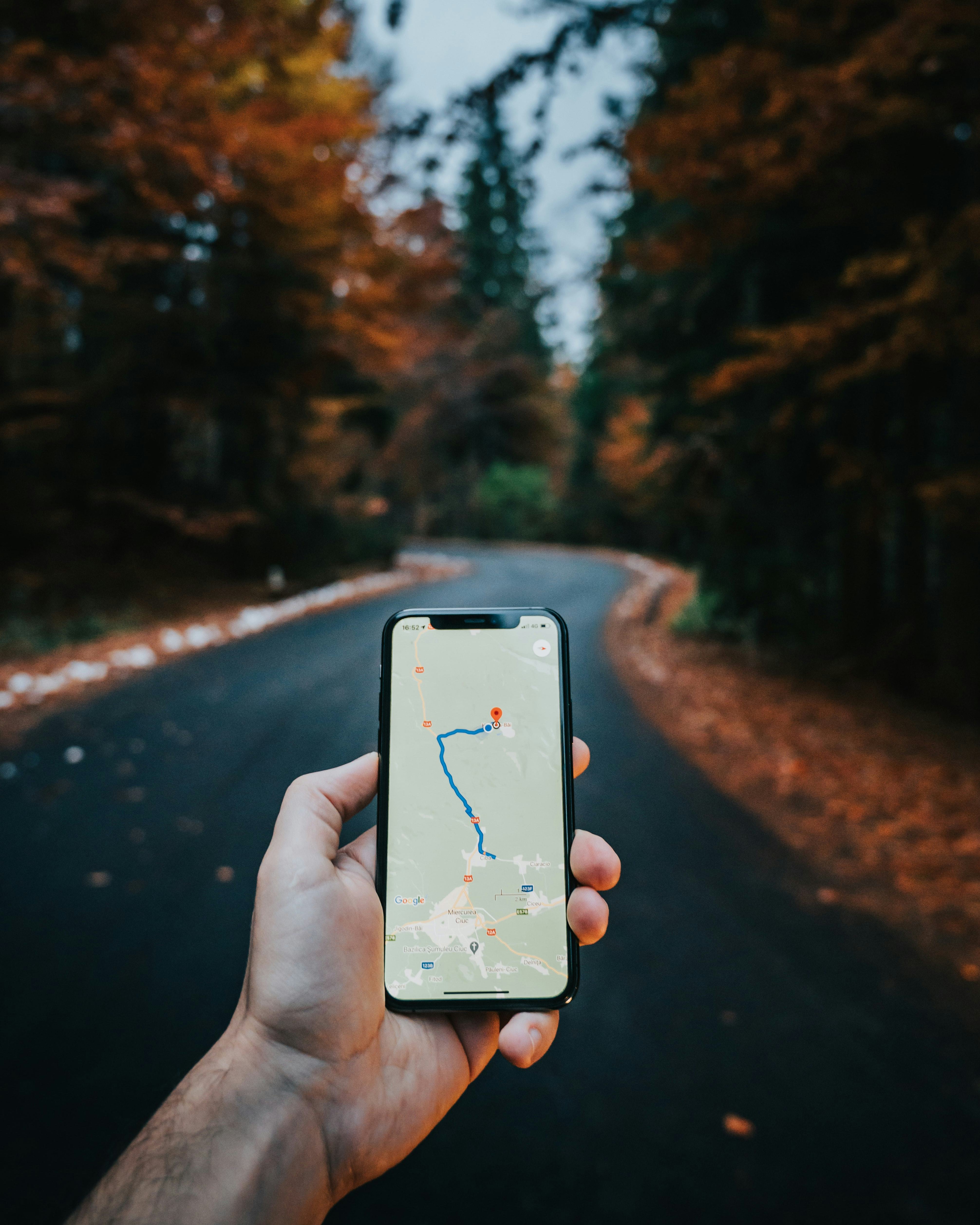Google Maps app in a man's hand with a country road and fall tress in the background