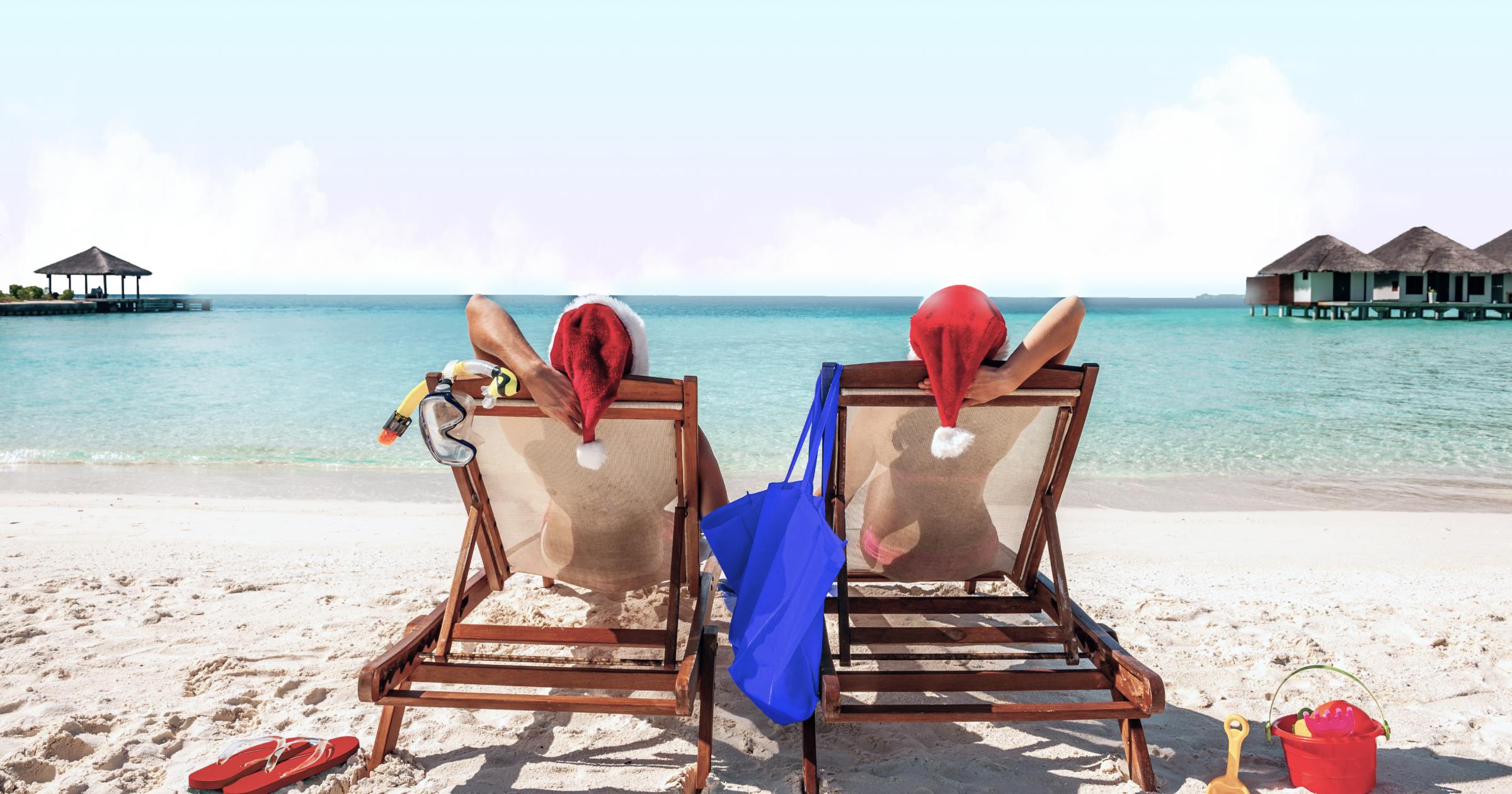 Two women with santa hats sitting on beach loungers facing the sea