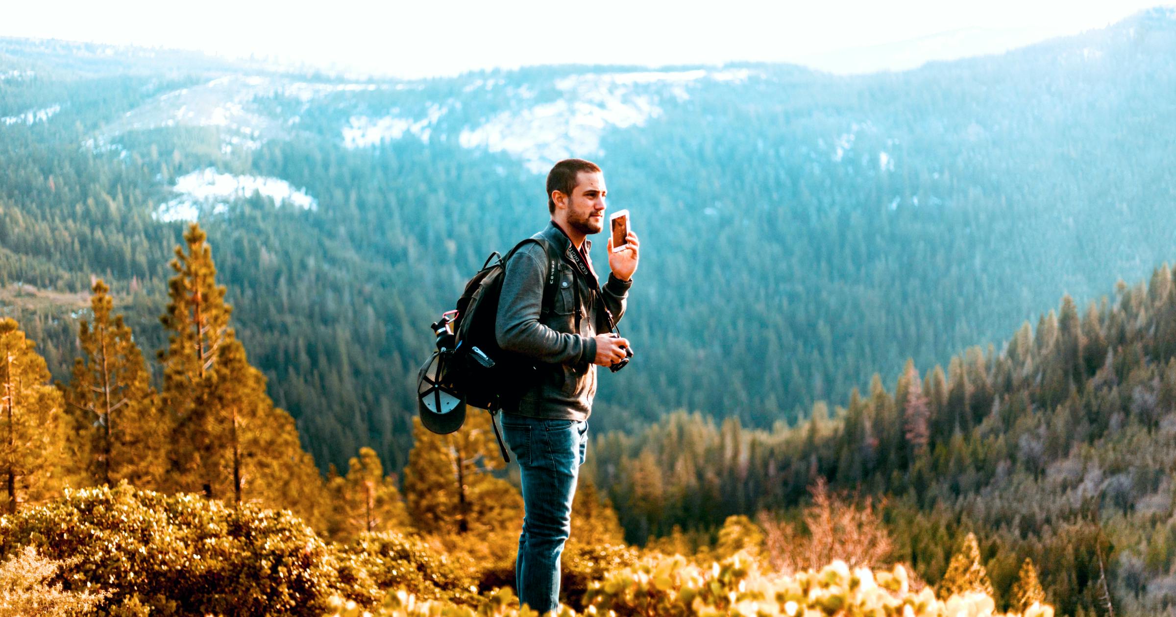 Image of a man talking on his cellphone while walking through the mountains with a backpack for Virtual SIM card blog