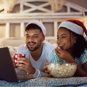 10 holiday movies to download before you fly with image of cute festive couple eating popcorn and watching a movie