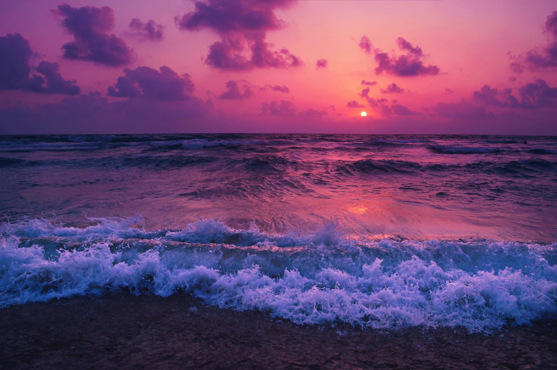Sunset over pink and purple sky with waves crashing
