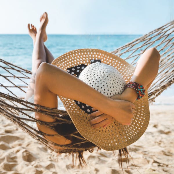 Woman in a wide brim hat on a hammock on the beach overlooking the ocean