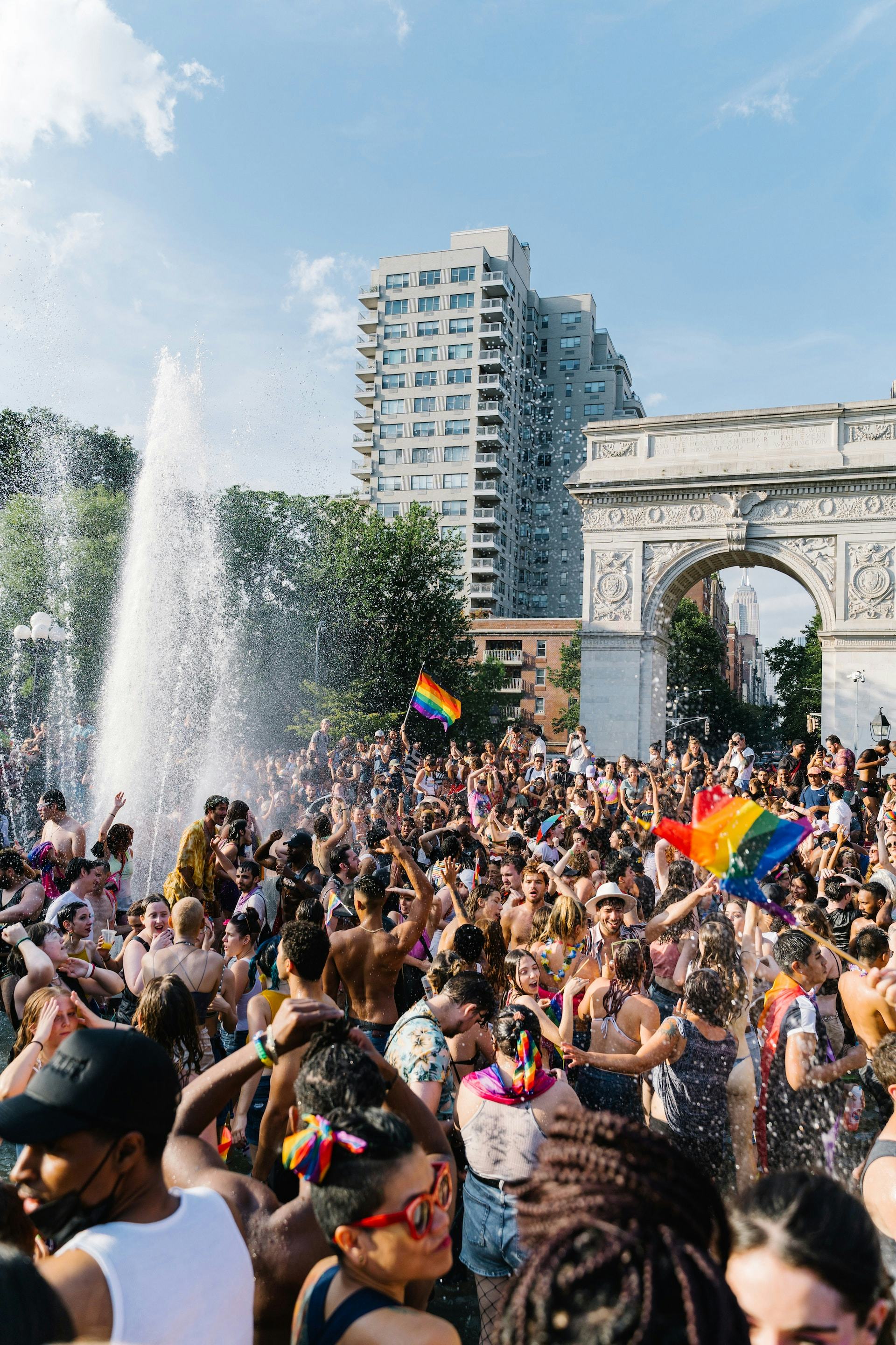People celebrating in Washington Square Park in New York City waving gay Pride flags.