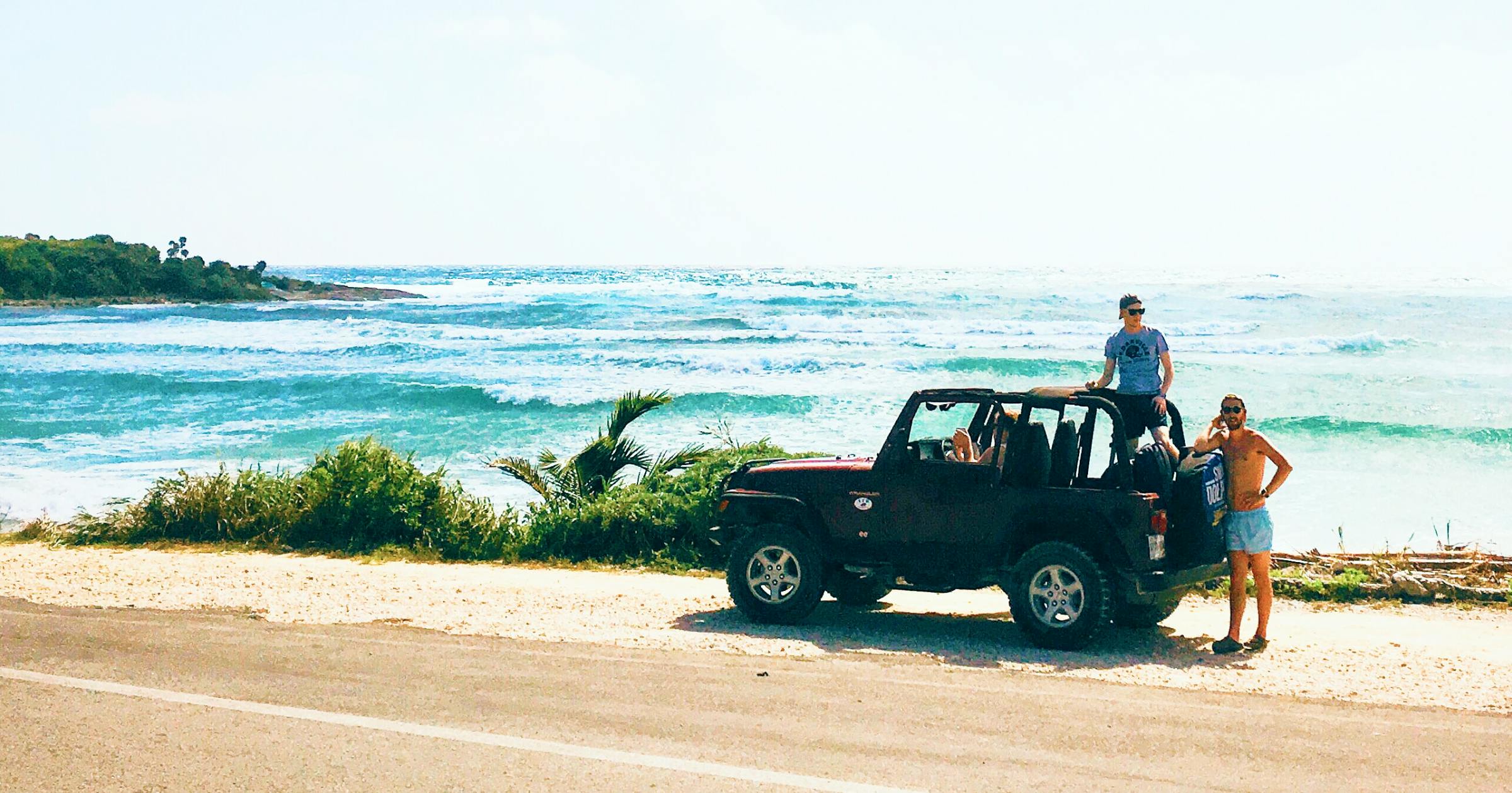 Jeep with two guys hanging out the back and waves and the beach in the background