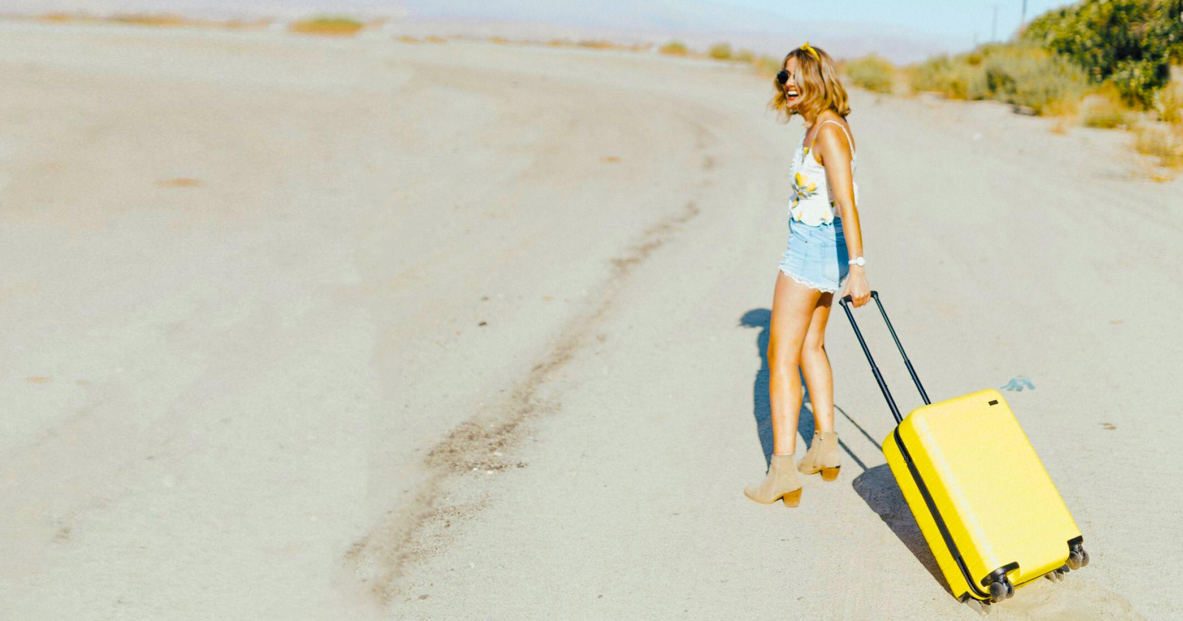 woman smiling on beach with yellow carry-on suitcase wide