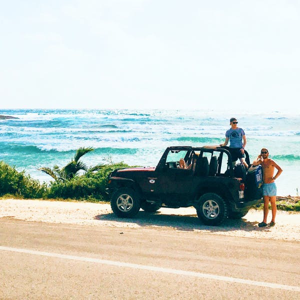 Jeep with two guys hanging out the back and waves and the beach in the background