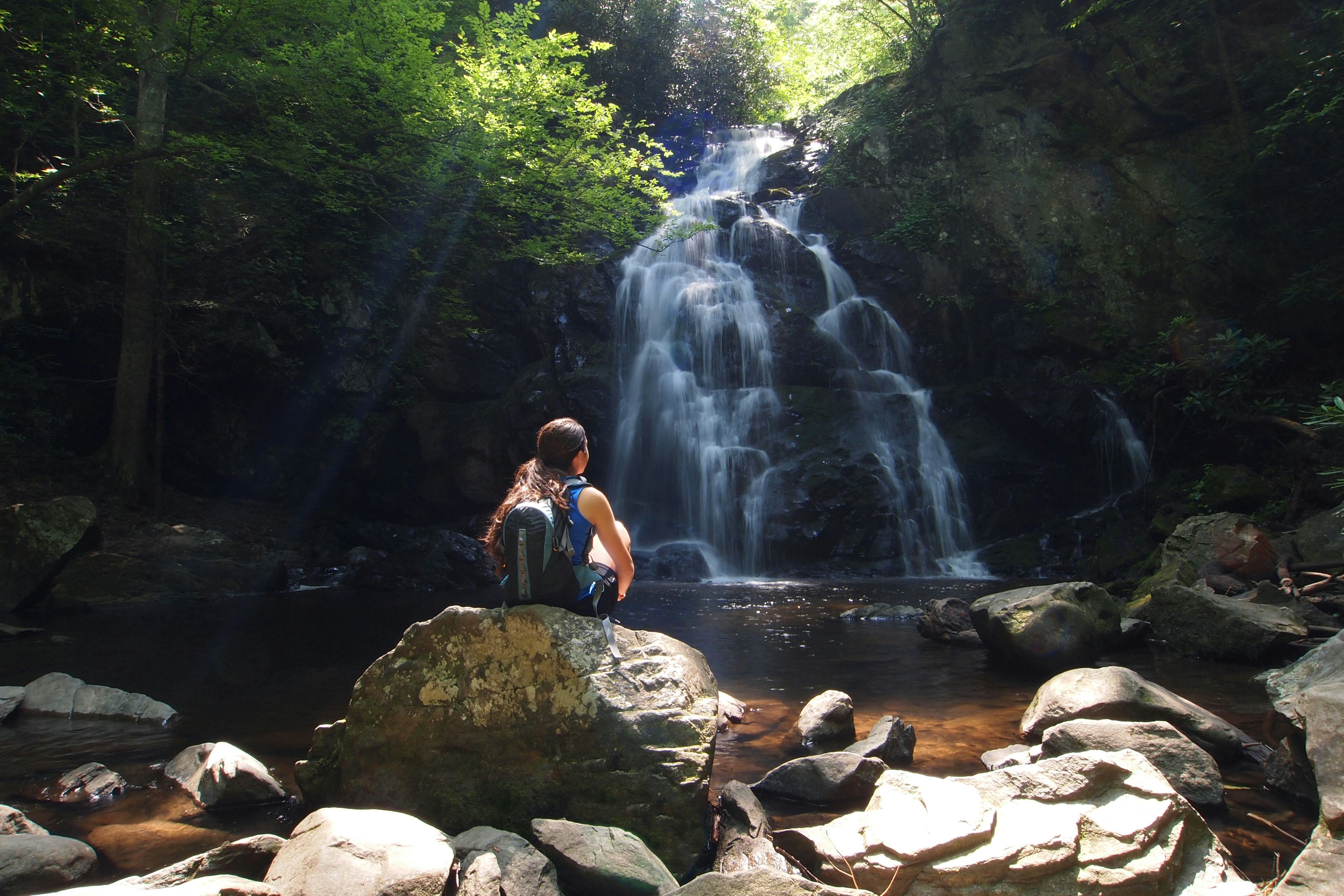 Girl sitting on some rocks looking at a waterfall in the  Great Smokey Mountains