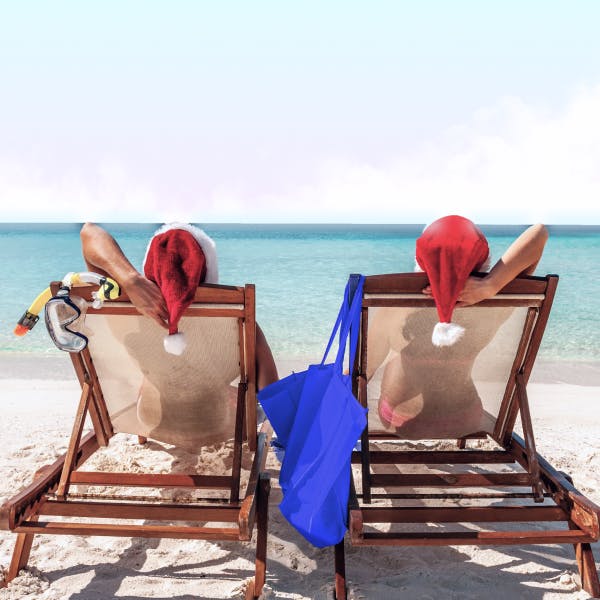 Two women with santa hats sitting on beach loungers facing the sea