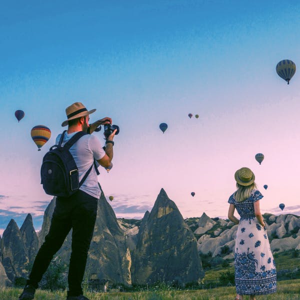 Man taking photos of a woman looking into a sky filled with hot air balloons and a cotton candy sky representing Influences to follow on Instagram 