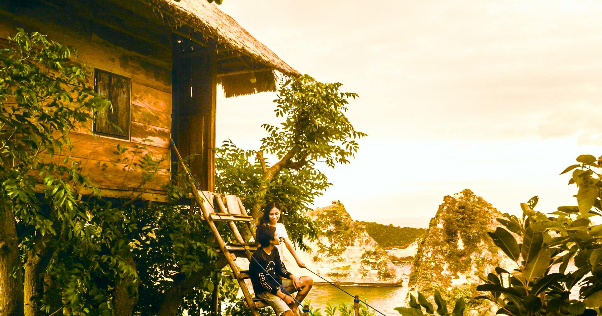 Couple sitting on stairs to a vacation rental treehouse on an island with water and greenery in the background