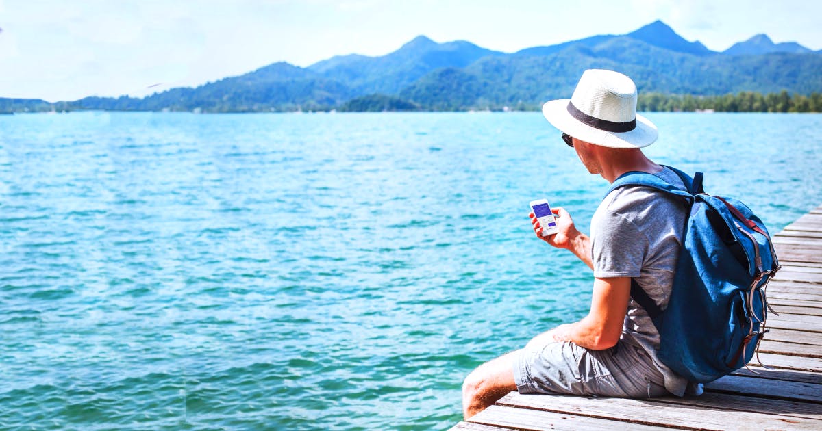 Man in grey shirt and pants with a white hat and blue backpack sitting on a dock looking at the Faye app