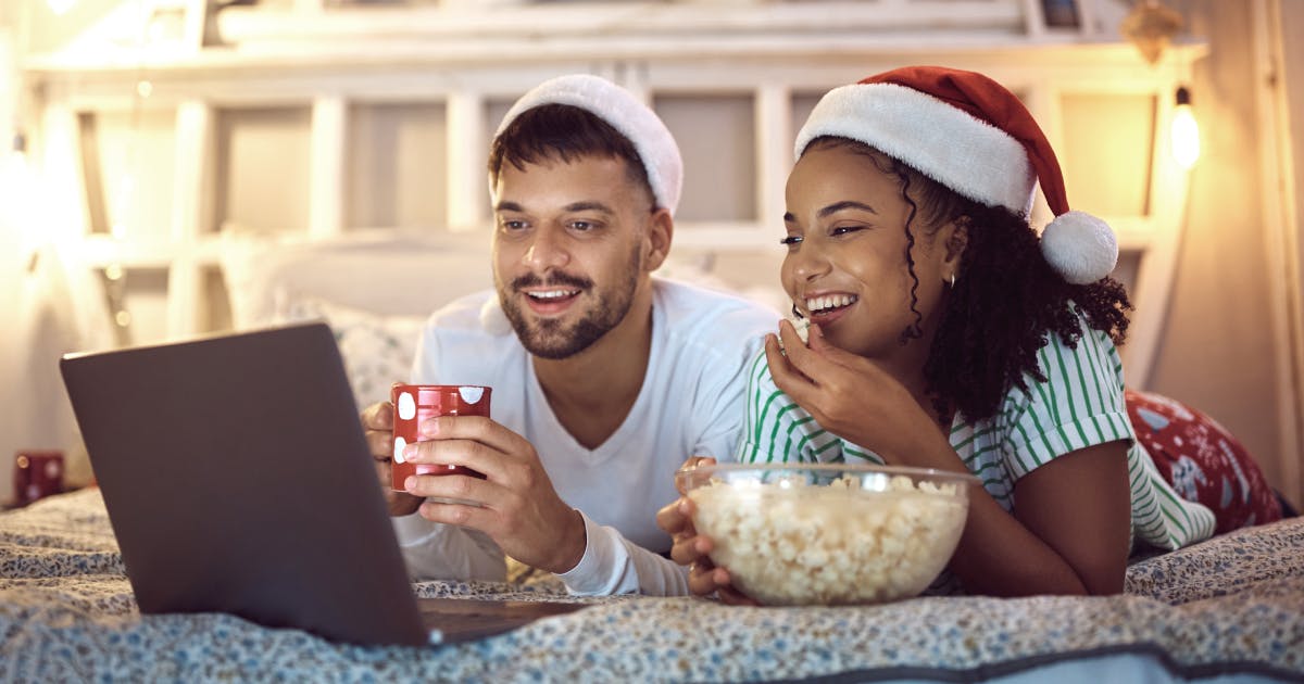 10-holiday movies to download before you fly with image of cute festive couple eating popcorn and watching a movie
