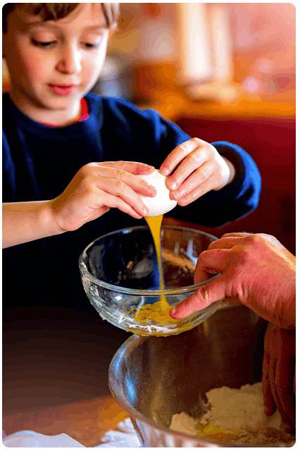 young boy cracks an egg into a glass mixing bowl