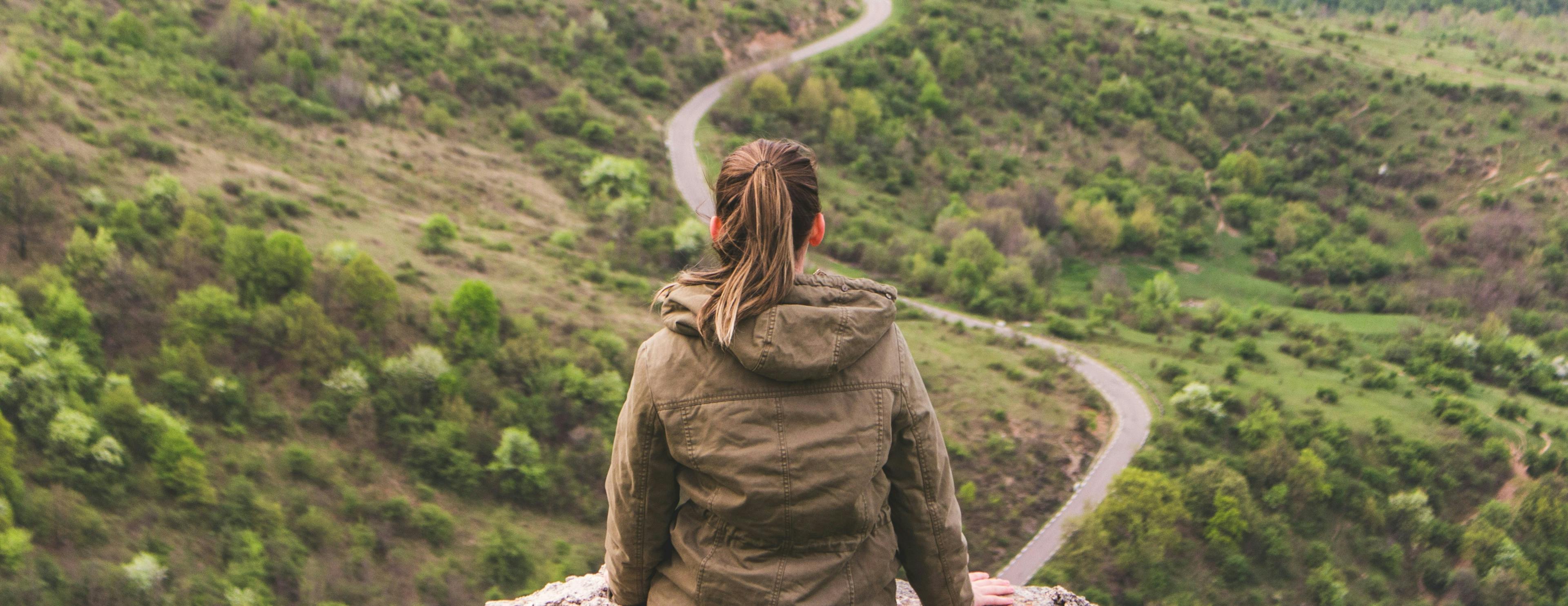 A woman sitting on a cliff looking at the road in front of her