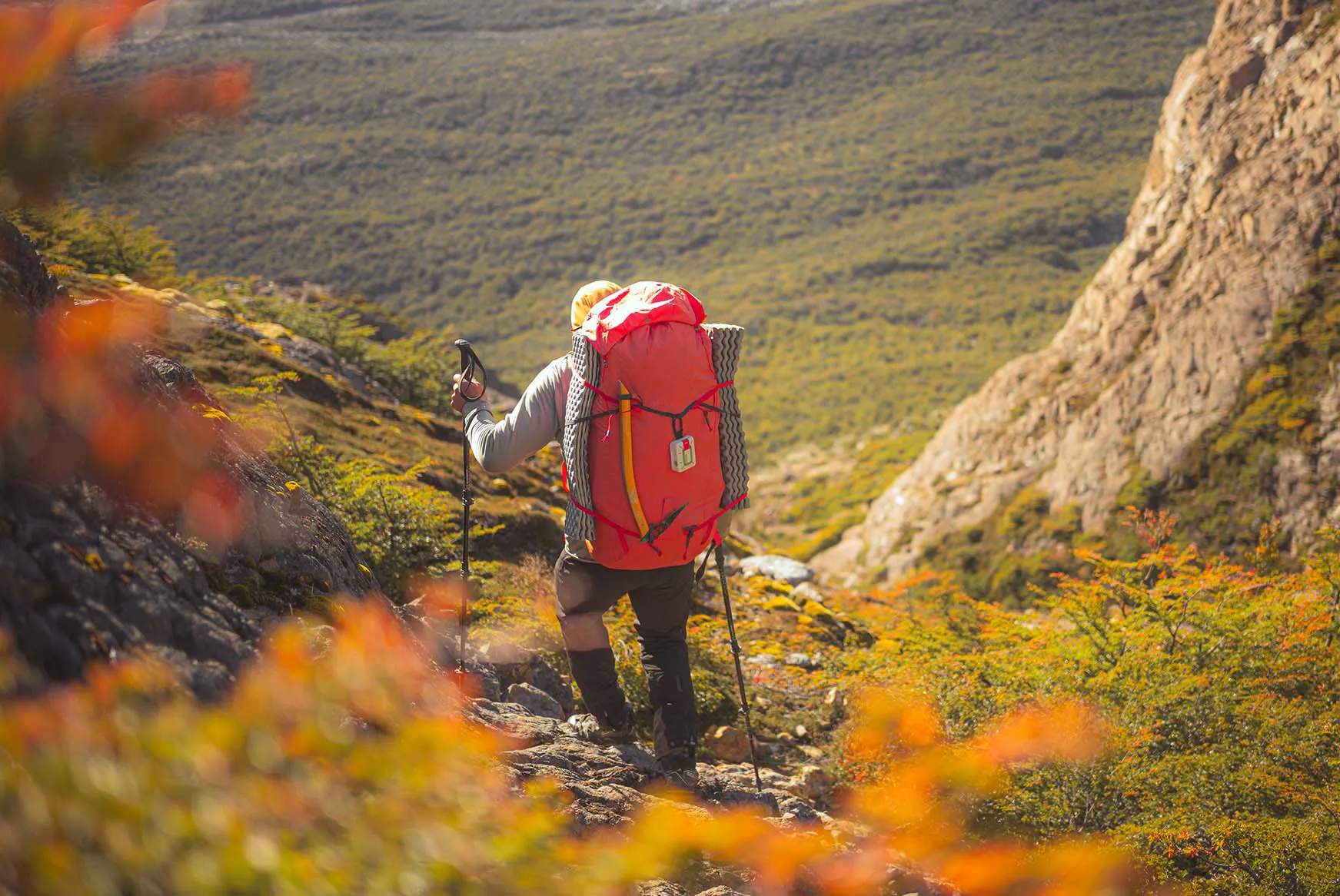 A hiker going down a mountain, wearing a ZOLEO on their backpack