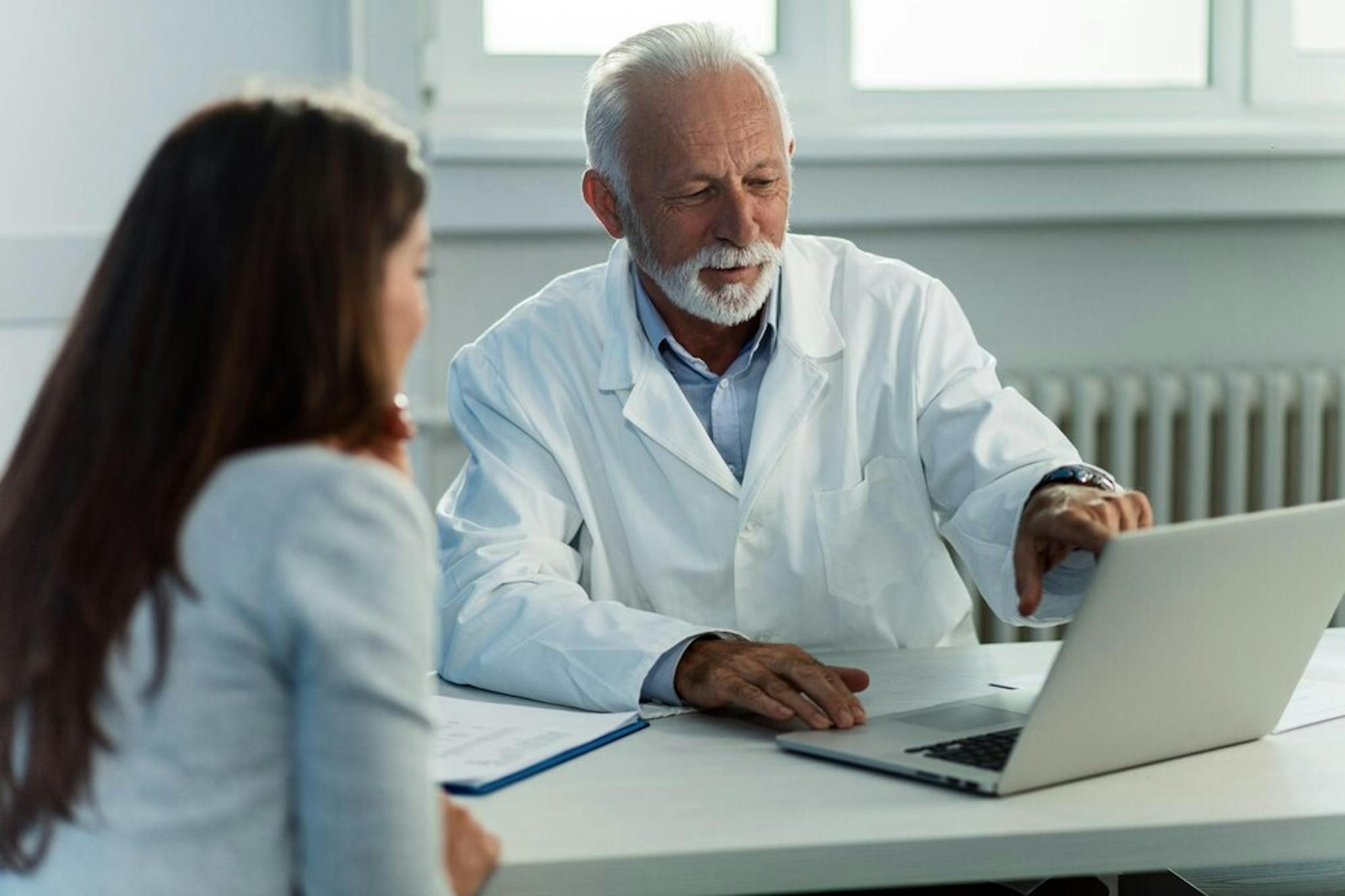 mature-doctor-and-his-patient-talking-while-reading-medical-record-on-computer