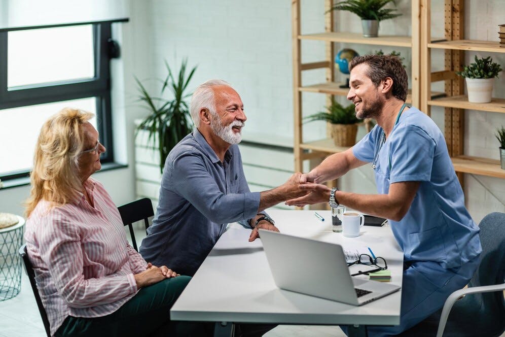 happy-male-doctor-shaking-hands-with-senior-man-who-came-medical-appointment-with-his-wife